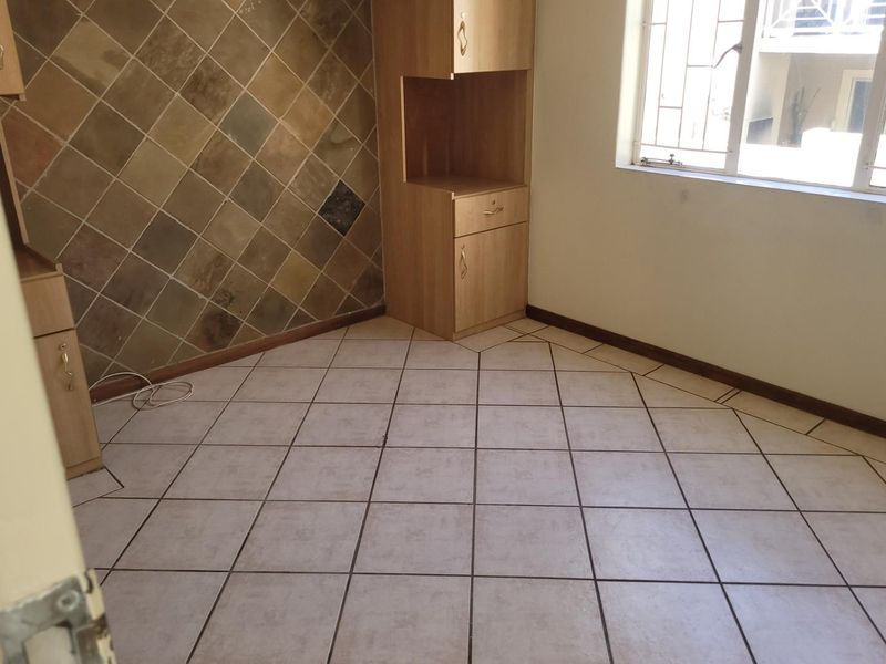 An empty bedroom featuring tiled flooring, a tiled feature wall, and built-in cabinetry, with security bars installed on the window.