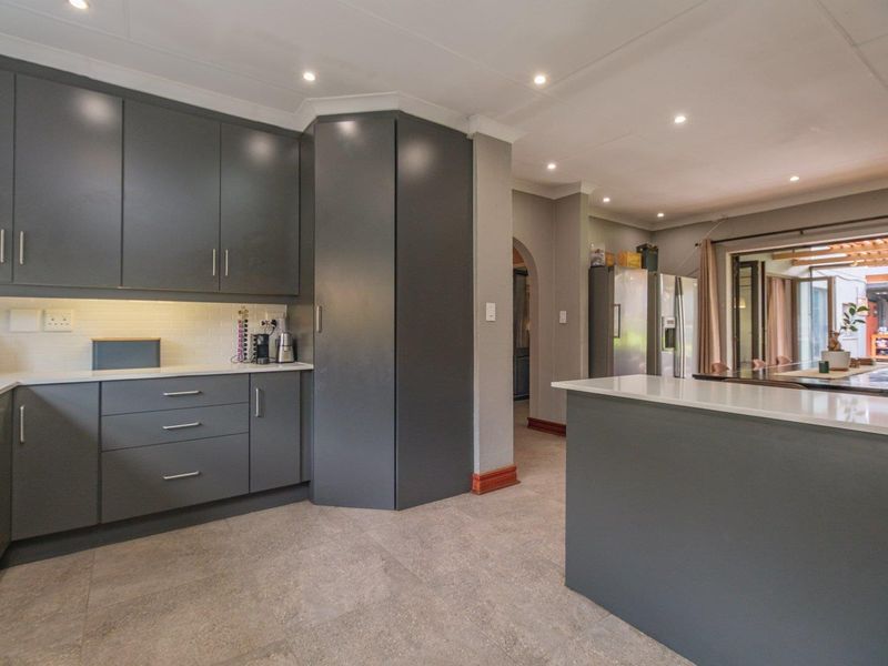 Modern kitchen featuring dark grey cabinetry, stone countertops, a central island, and tiled flooring, seamlessly flowing into the adjacent living area.