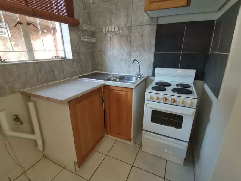 Compact kitchen featuring a stainless steel sink, tiled splashback, and a freestanding electric stove with built-in cabinetry.