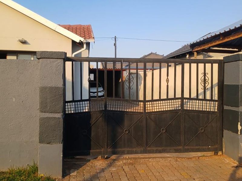 Front view of the property featuring a metal driveway gate, paved driveway, and masonry boundary walls.