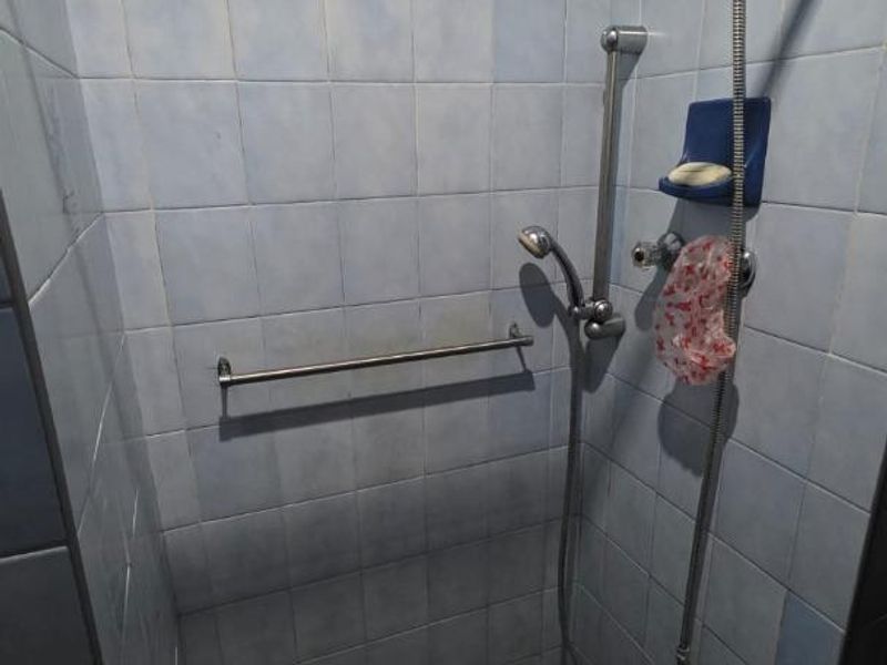 A shower enclosure featuring blue wall tiles, a mosaic tiled floor, and a wall-mounted shower mixer with a handheld shower head.