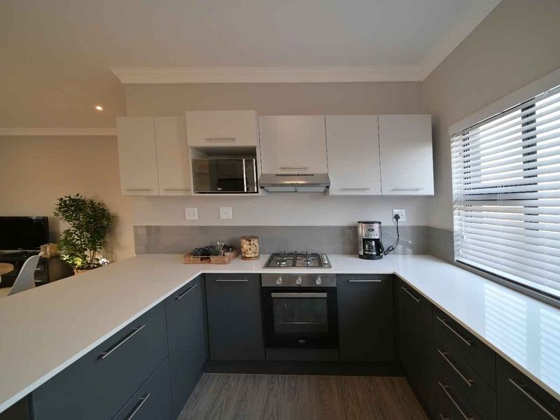 Modern kitchen featuring grey cabinetry, white quartz countertops, built-in oven, gas hob, extractor fan, and a subway tile backsplash.