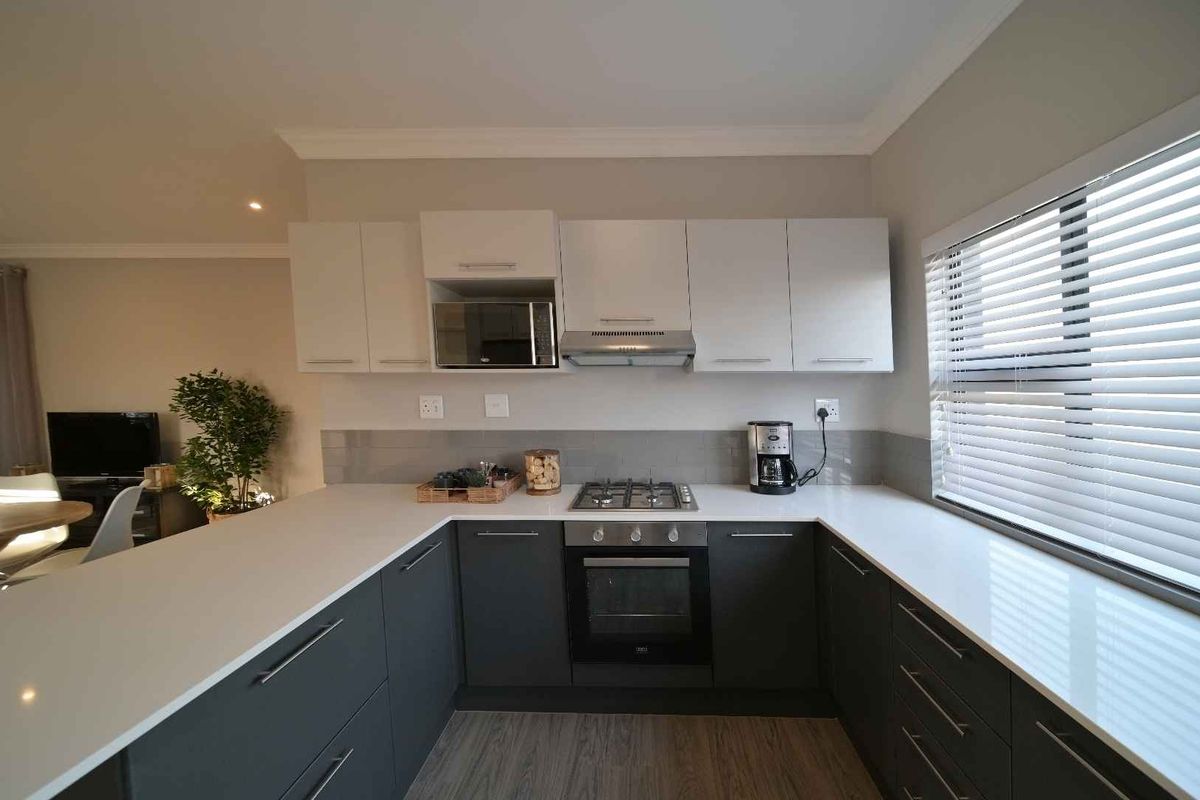 Modern kitchen featuring grey cabinetry, white quartz countertops, built-in oven, gas hob, extractor fan, and a subway tile backsplash.