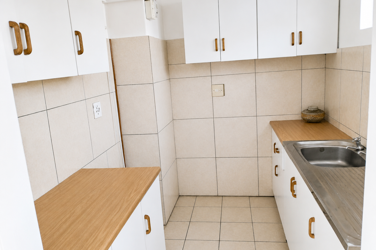 A compact, functional kitchen featuring white cabinetry, wood-look laminate countertops, a stainless steel sink, and neutral tiled finishes throughout.