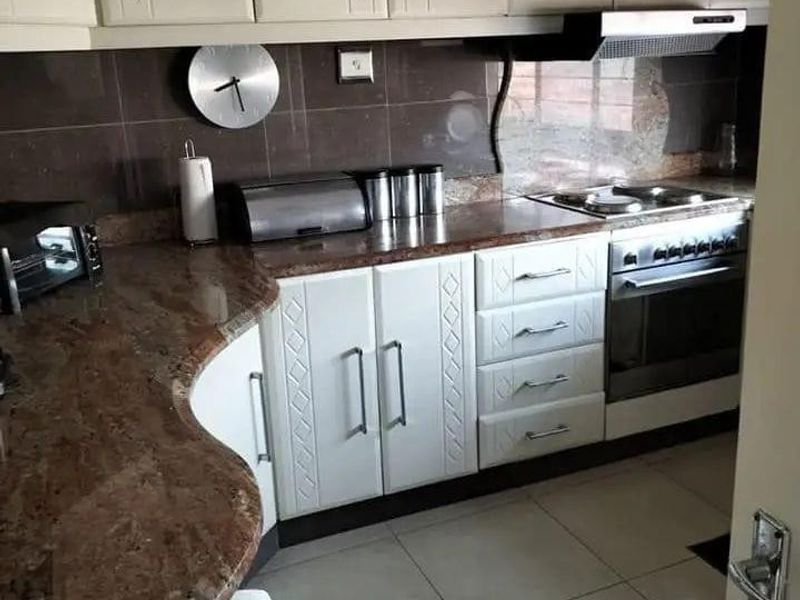 A functional kitchen featuring granite countertops, fitted cabinetry, a built-in oven with extractor fan, and tiled flooring.