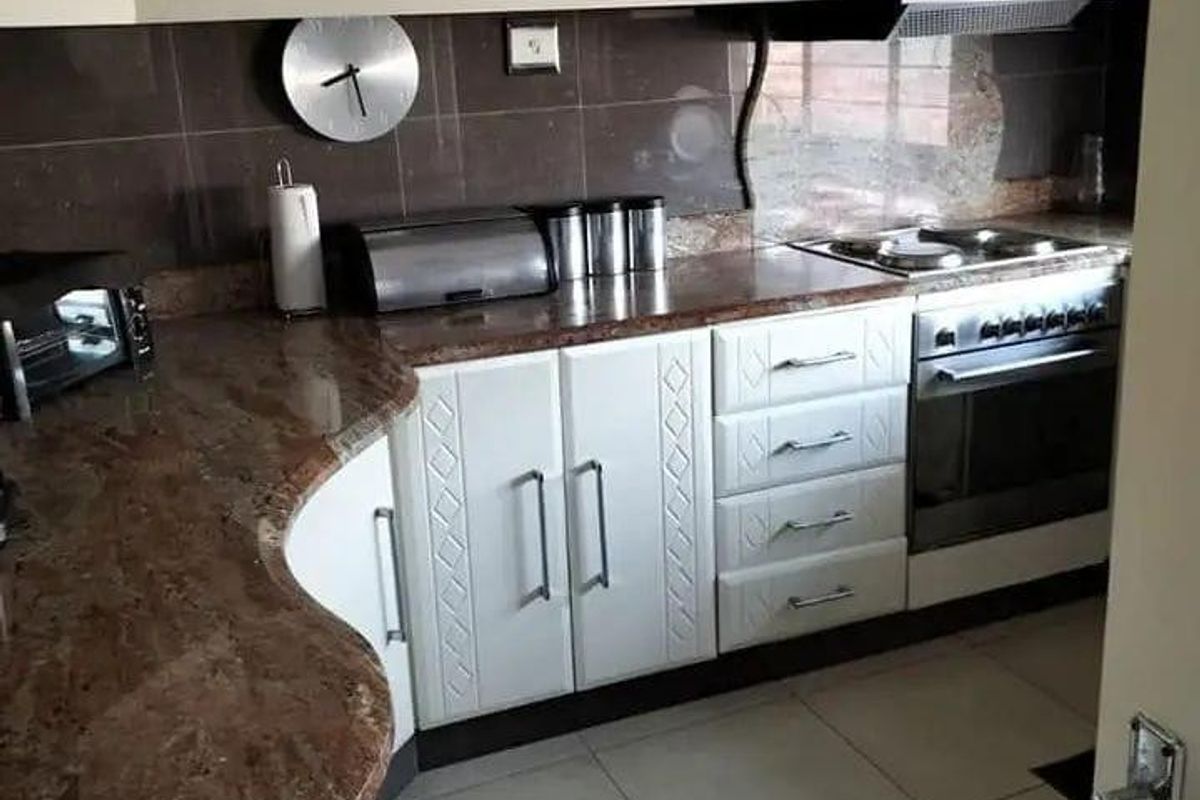 A functional kitchen featuring granite countertops, fitted cabinetry, a built-in oven with extractor fan, and tiled flooring.