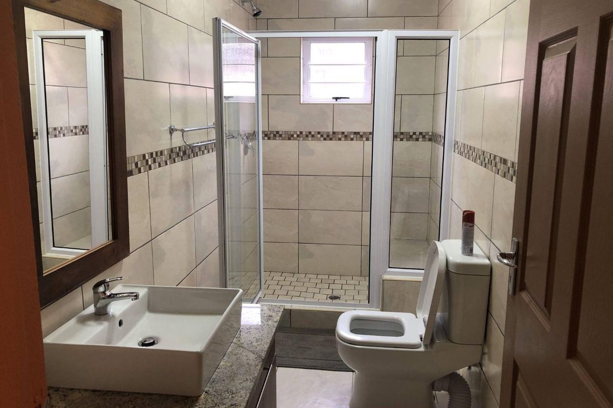 A modern bathroom featuring a tiled walk-in shower, a vessel sink set on a granite vanity top, and a standard toilet.