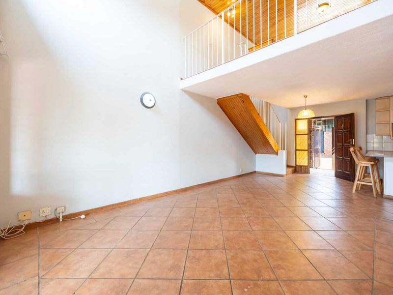 Spacious open-plan living area featuring a double-volume ceiling, mezzanine level, tiled flooring, and an integrated kitchen with breakfast counter.