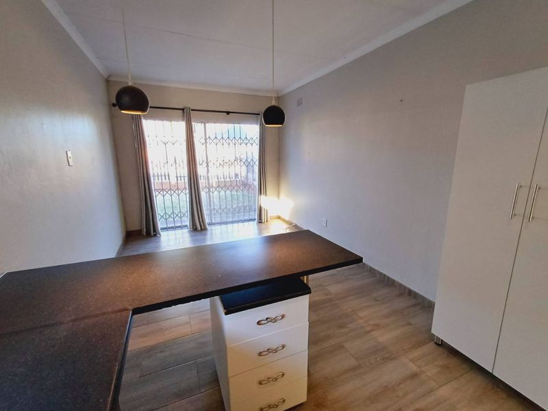 A bright, open-plan living area featuring laminate flooring, modern pendant lighting, and a sliding glass door with security gate leading to the exterior.