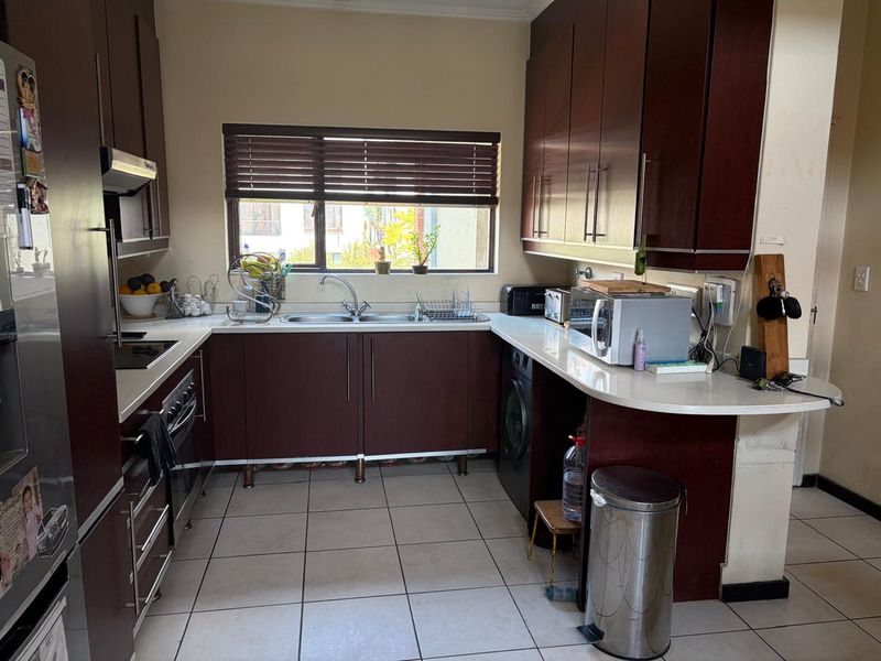 A functional kitchen featuring dark wood cabinetry, white stone countertops, integrated appliances, and tiled flooring with a window providing natural light.