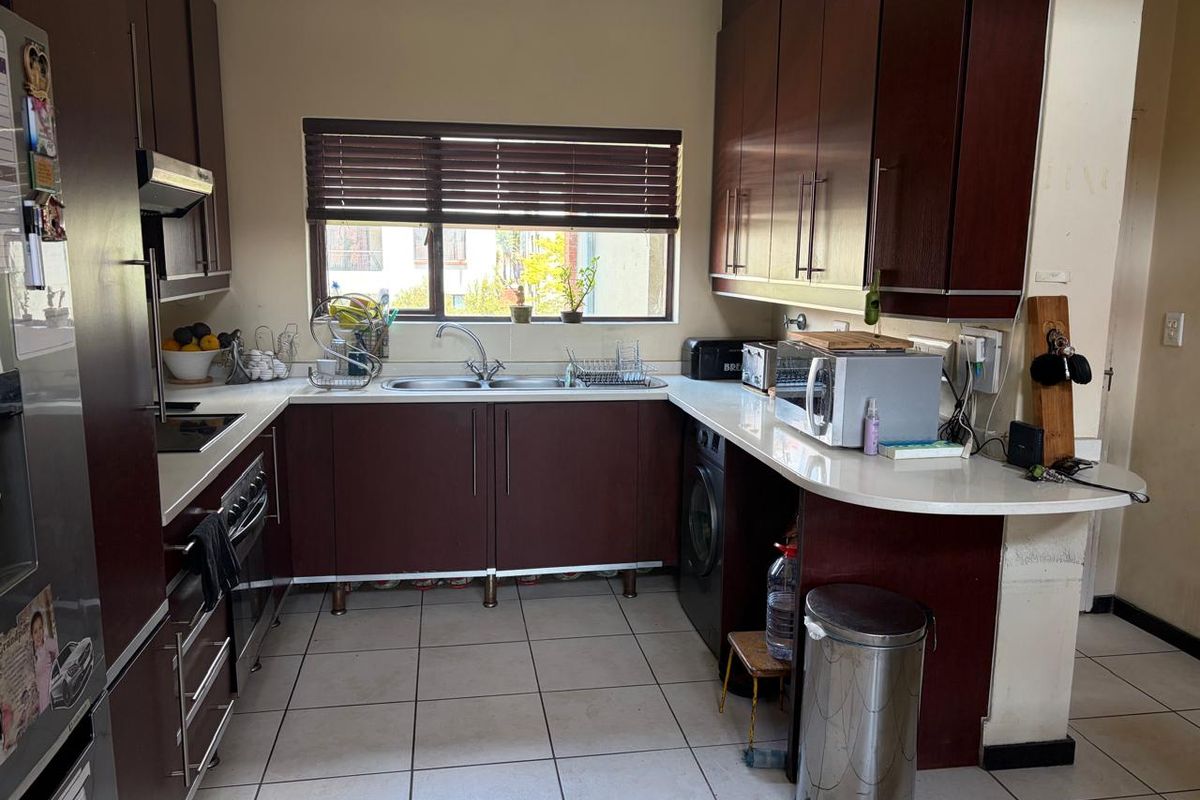 A functional kitchen featuring dark wood cabinetry, white stone countertops, integrated appliances, and tiled flooring with a window providing natural light.