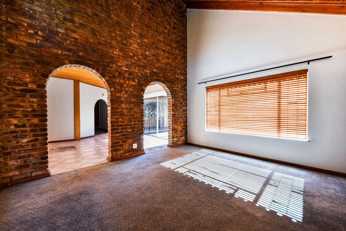 Spacious living area featuring a striking exposed brick wall, arched architectural details, vaulted ceilings with timber beams, and natural light through venetian blinds.