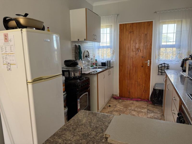 A functional kitchen featuring tiled flooring, laminate countertops, built-in cabinetry, and a freestanding stove, offering potential for modernization and aesthetic updates.
