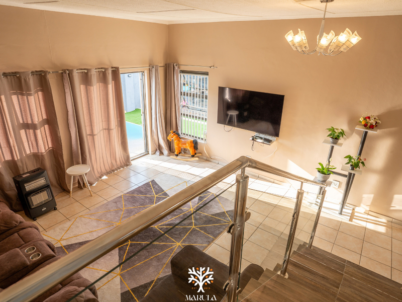 Spacious living area featuring tiled floors, a modern stainless steel balustrade, and direct access to an outdoor patio through sliding glass doors.