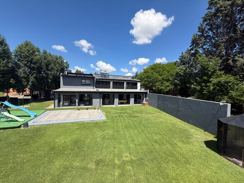 Rear view of a modern two-story house featuring a spacious lawn, covered patio area, balcony, and boundary wall.