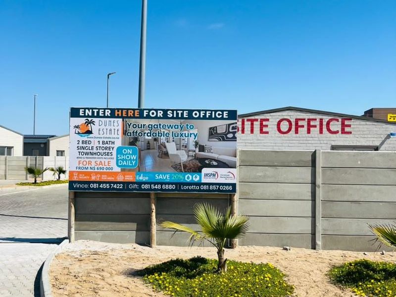Exterior view of the estate site office entrance featuring a paved driveway, boundary wall, and promotional signage for the townhouse development.