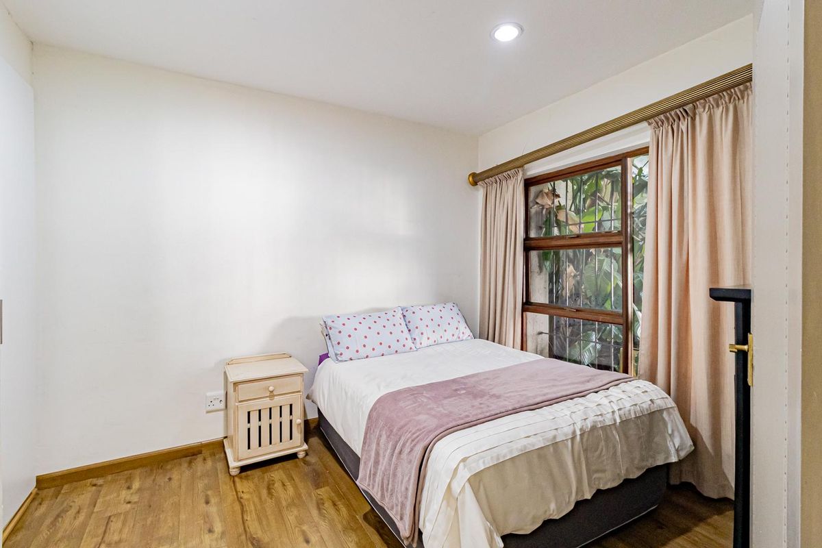 A bedroom featuring wood-look flooring, recessed ceiling lighting, and a large window with security bars overlooking greenery.
