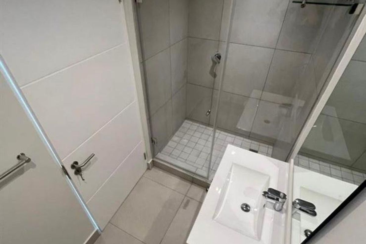 Modern bathroom featuring a glass-enclosed shower, wall-mounted vanity with basin, and neutral floor-to-ceiling tiling.