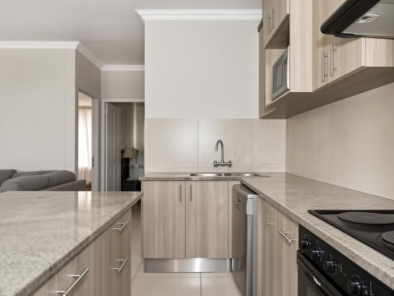 Modern kitchen featuring light wood-tone cabinetry, stone-look countertops, integrated appliances, and a clean tiled splashback, seamlessly flowing into the adjacent living area.