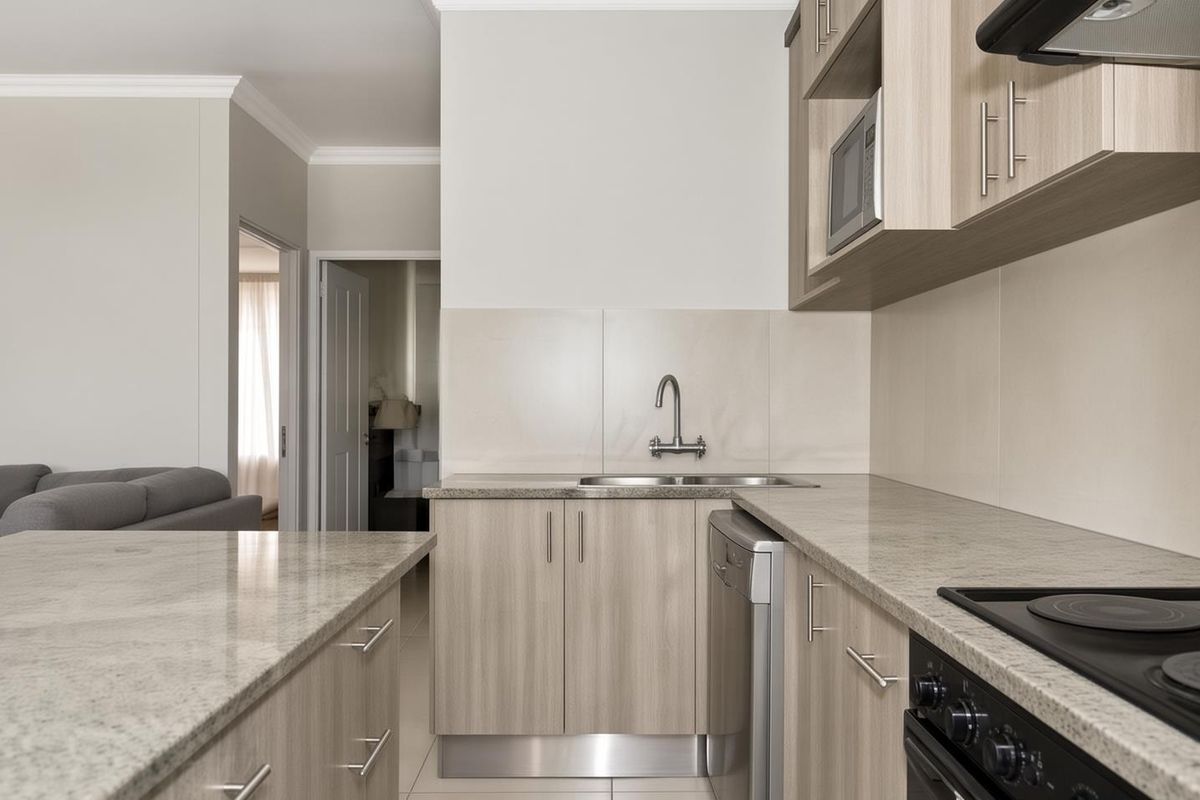Modern kitchen featuring light wood-tone cabinetry, stone-look countertops, integrated appliances, and a clean tiled splashback, seamlessly flowing into the adjacent living area.