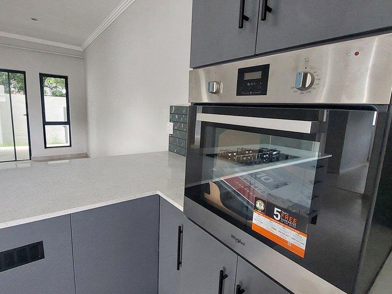 Modern kitchen featuring sleek grey cabinetry, high-quality quartz countertops, and a built-in Whirlpool oven in an open-plan layout.