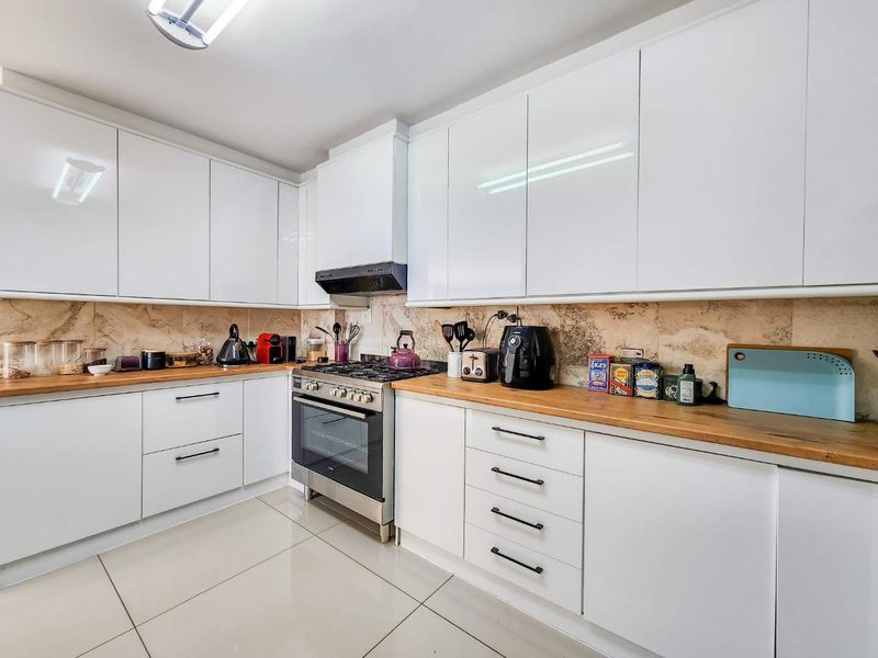 Modern kitchen featuring white gloss cabinetry, wooden countertops, stainless steel gas stove, extractor fan, and tiled backsplash.