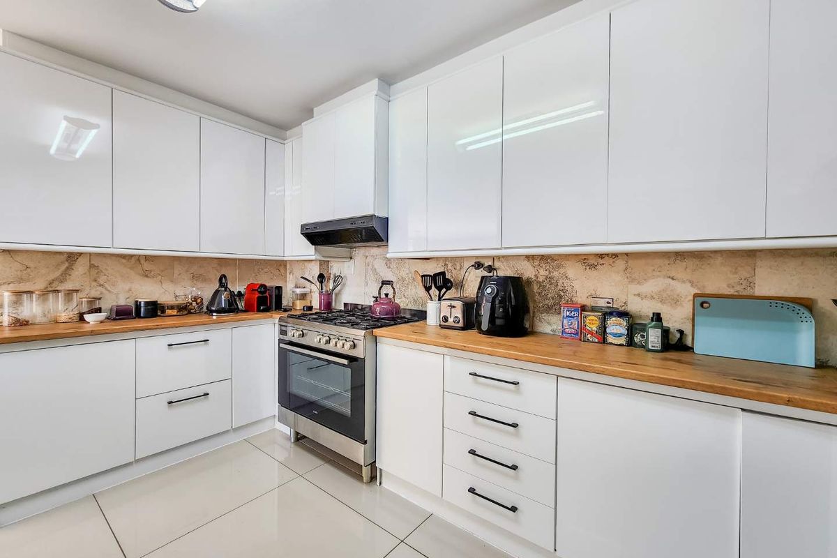 Modern kitchen featuring white gloss cabinetry, wooden countertops, stainless steel gas stove, extractor fan, and tiled backsplash.