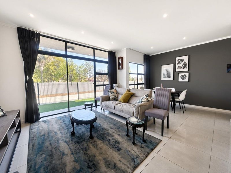 A bright open-plan living and dining area featuring large sliding glass doors, neutral tiled flooring, and a modern dark accent wall.