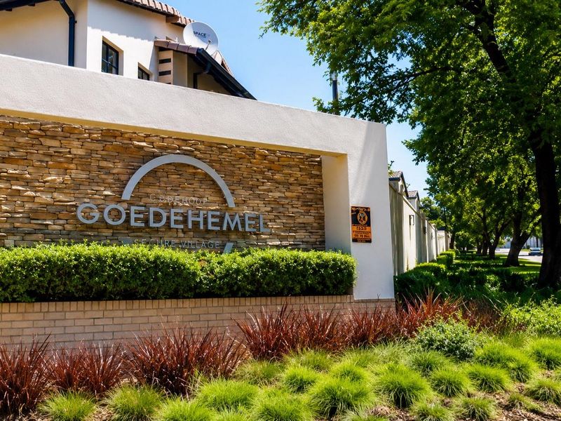 Entrance signage and stone-clad boundary wall for Goedehemel Secure Village, featuring well-maintained landscaping and perimeter fencing.