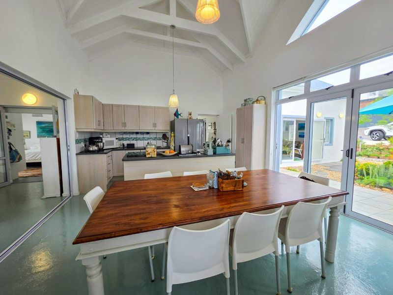 Spacious open-plan kitchen and dining area featuring a high vaulted ceiling with exposed rafters, modern cabinetry, and large sliding doors leading to the patio.