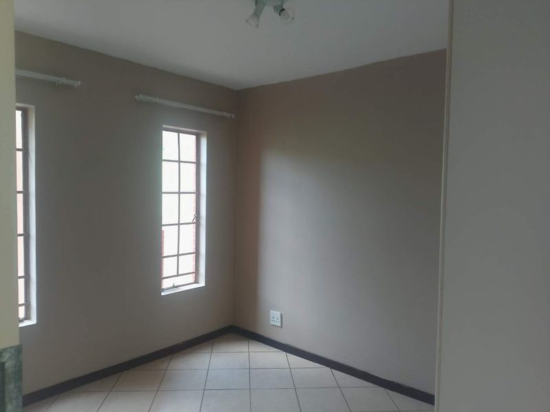An empty bedroom featuring neutral-toned walls, tiled flooring, and grid-pattern windows, providing a clean and versatile space ready for personalization.