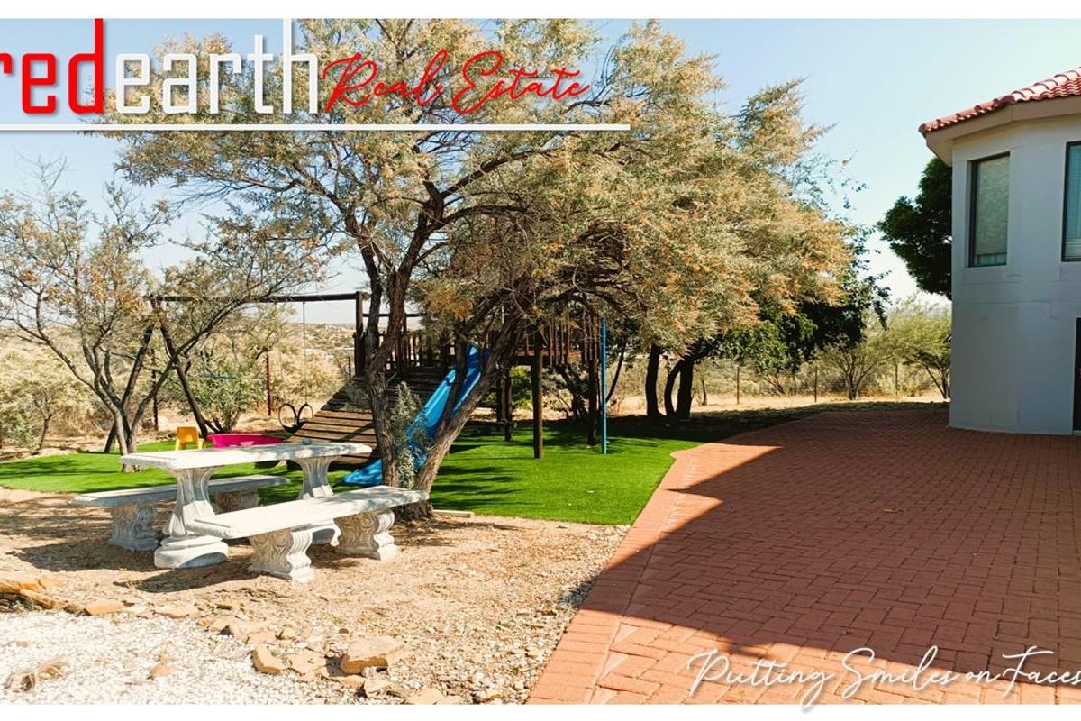 A spacious rear garden area featuring a paved patio, artificial lawn, and a built-in children's play structure set against the rear elevation of the house.