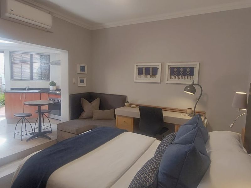 An open-plan bedroom and kitchen area featuring a built-in desk, split-system air conditioning, and functional kitchen cabinetry with tiled flooring.