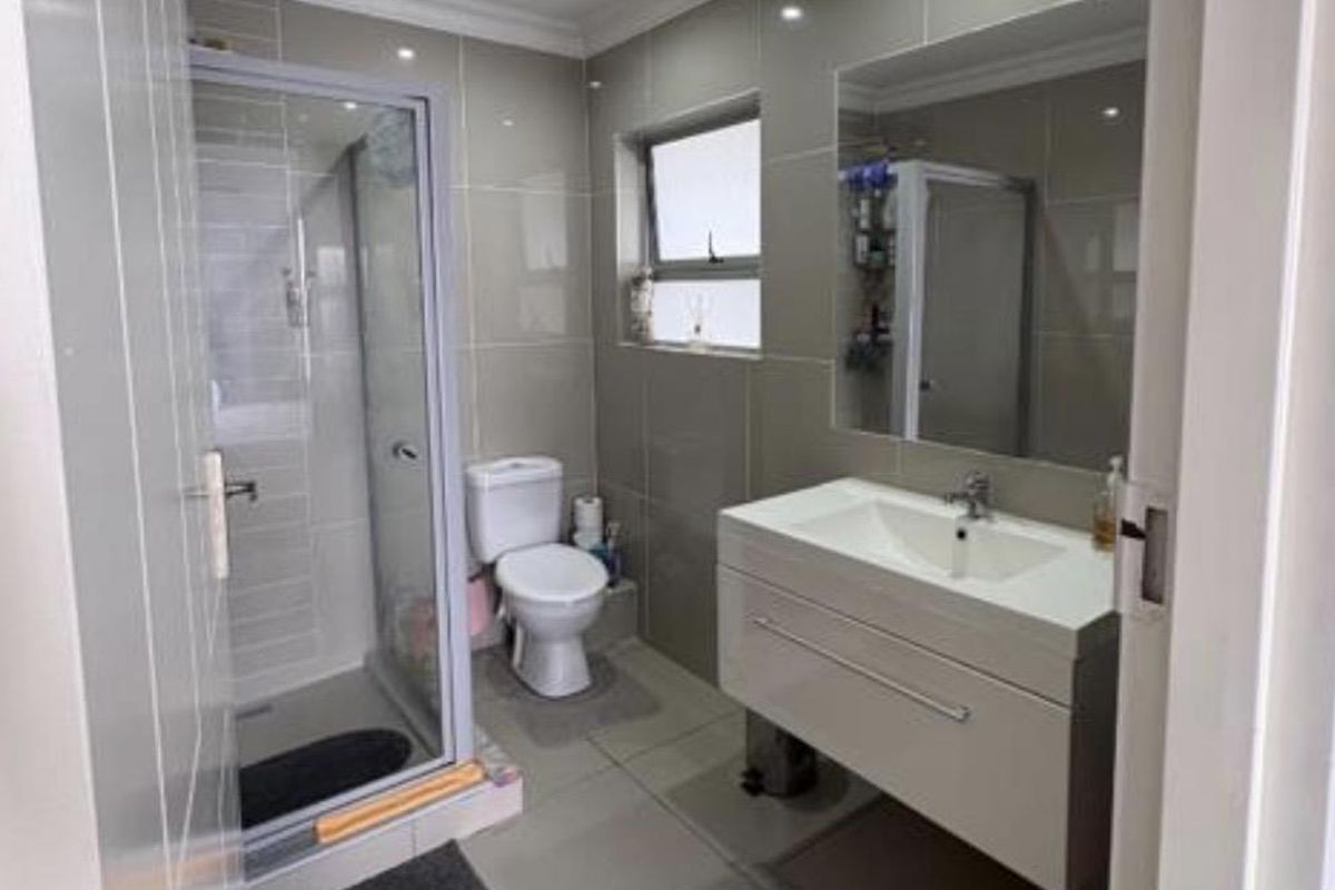 Modern bathroom featuring a glass-enclosed shower, wall-mounted vanity with integrated basin, large mirror, and tiled finishes throughout.