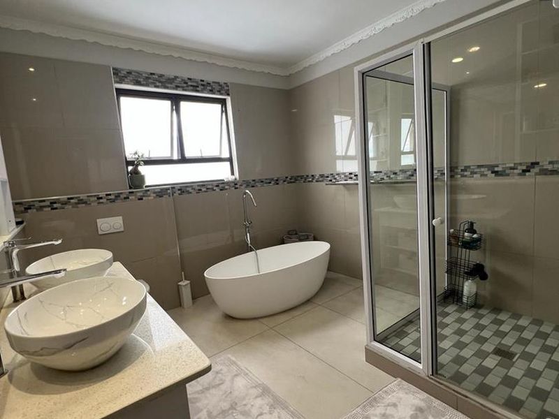 Modern bathroom featuring a freestanding bathtub, glass-enclosed shower, and double vanity with vessel sinks, finished with neutral tiling and a decorative mosaic border.