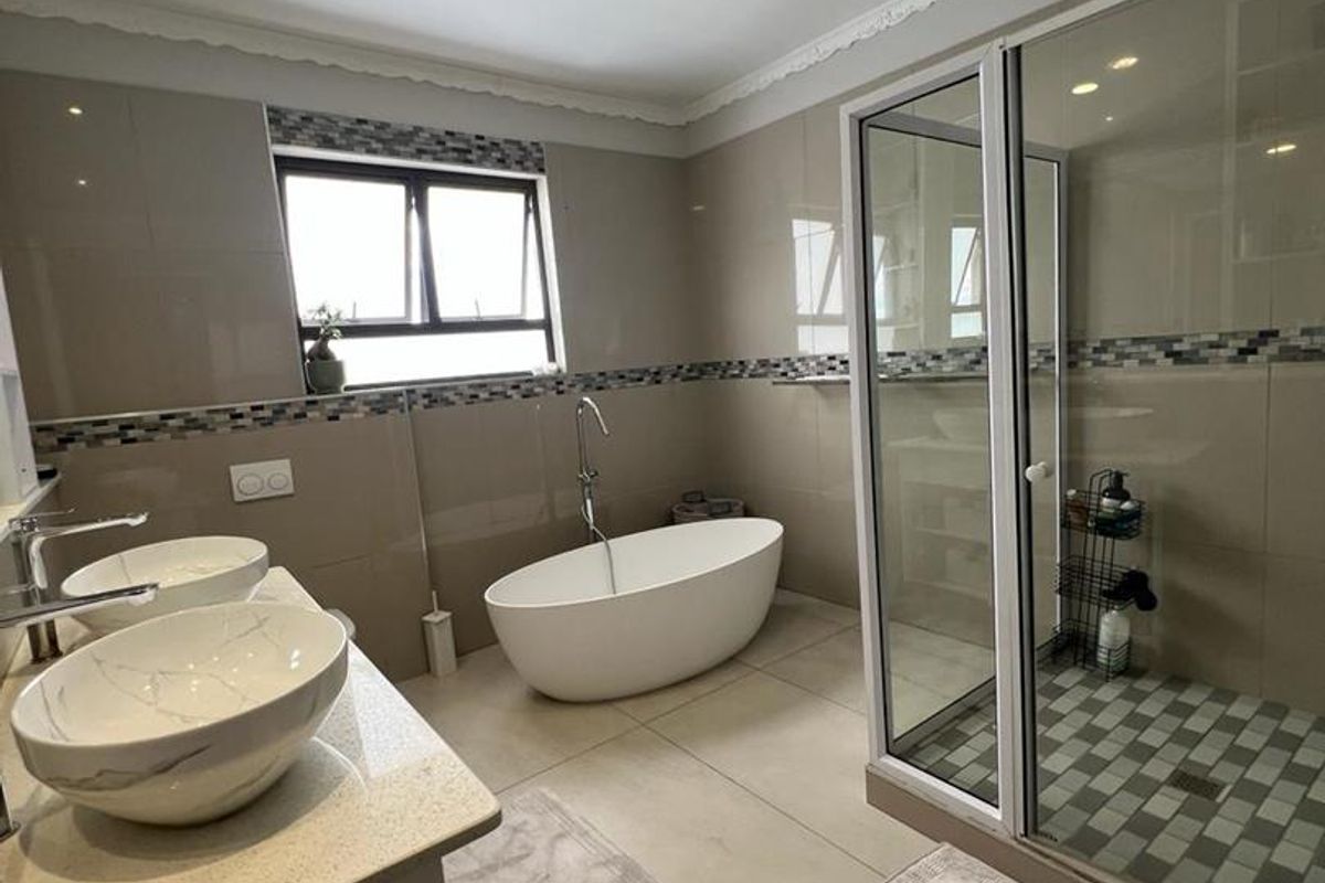 Modern bathroom featuring a freestanding bathtub, glass-enclosed shower, and double vanity with vessel sinks, finished with neutral tiling and a decorative mosaic border.