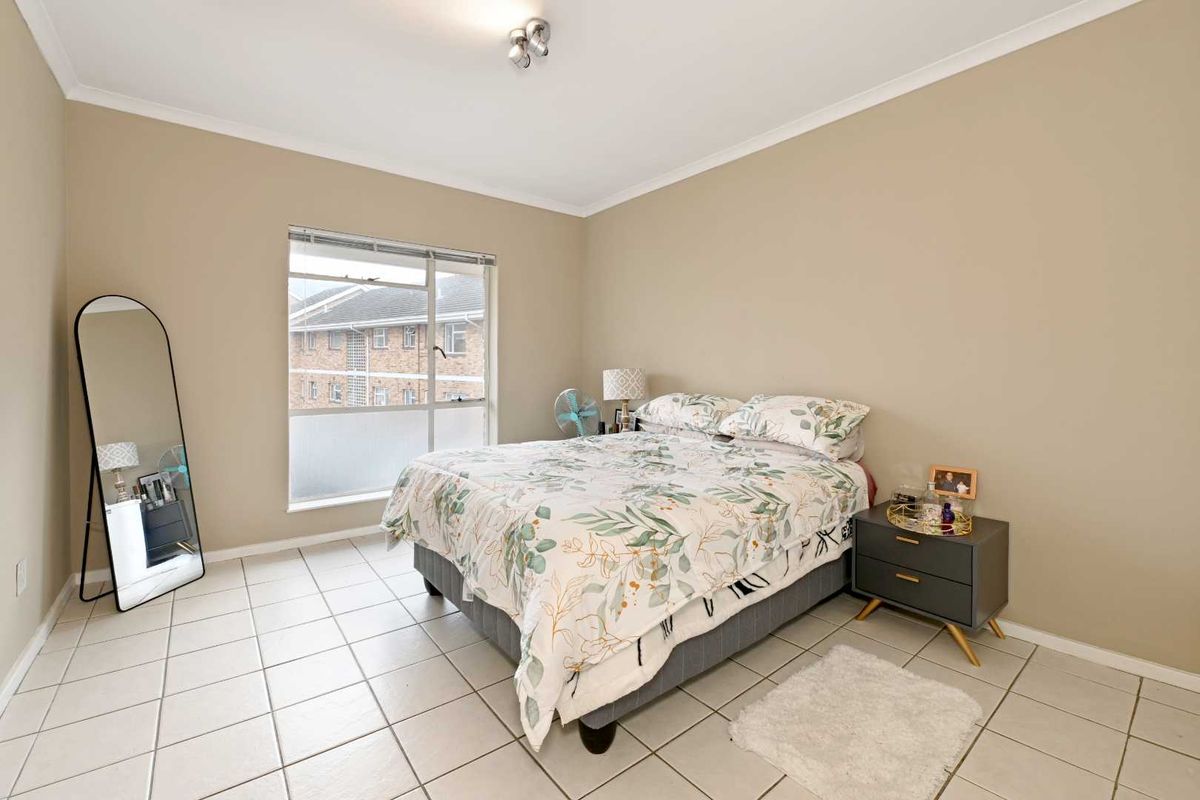 A well-lit bedroom featuring neutral wall tones, tiled flooring, and a large window providing natural light.