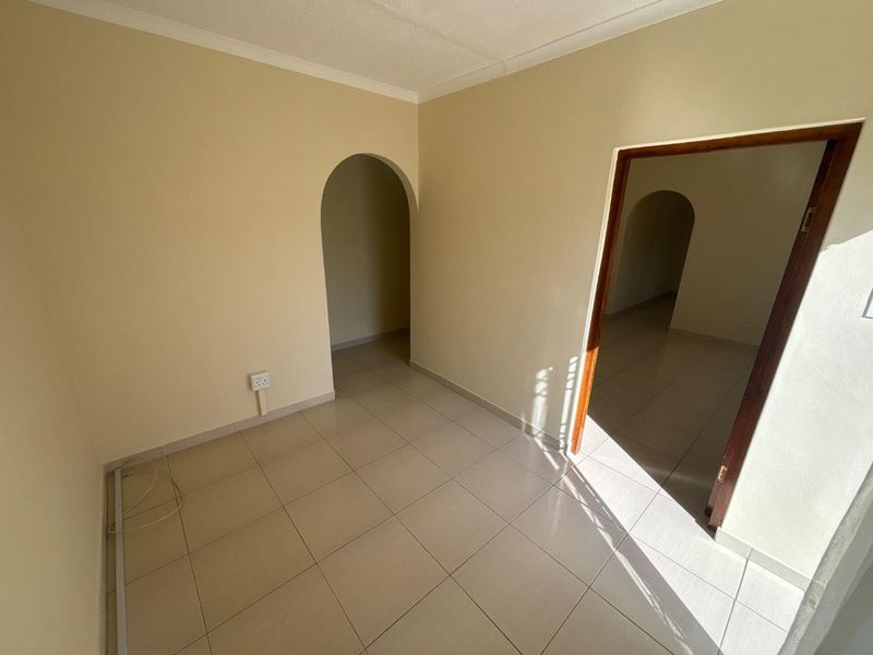 An empty living area featuring neutral tiled flooring, coved ceiling cornices, and an arched doorway leading to an adjacent space.