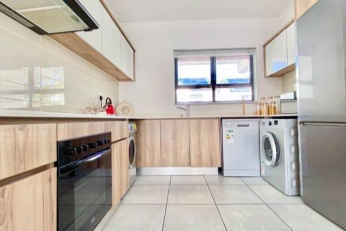 Modern kitchen featuring light wood-tone cabinetry, integrated appliances, tiled flooring, and a functional layout with ample storage and workspace.