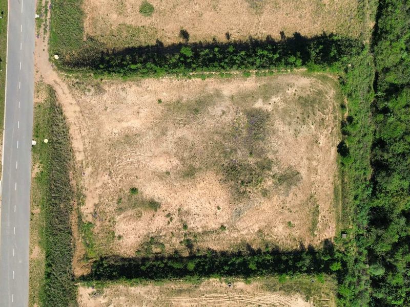 An aerial view of a vacant, cleared industrial land parcel with direct access to an adjacent paved road.