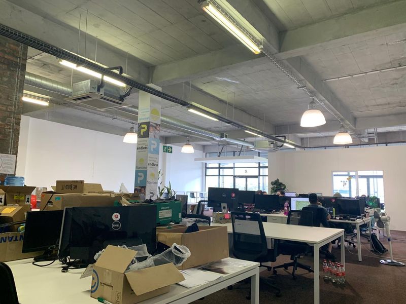 Open-plan office space featuring an industrial aesthetic with exposed concrete ceilings, ducting, and brickwork, providing a functional workspace environment.