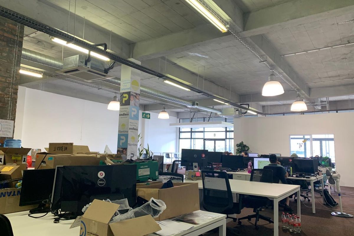 Open-plan office space featuring an industrial aesthetic with exposed concrete ceilings, ducting, and brickwork, providing a functional workspace environment.
