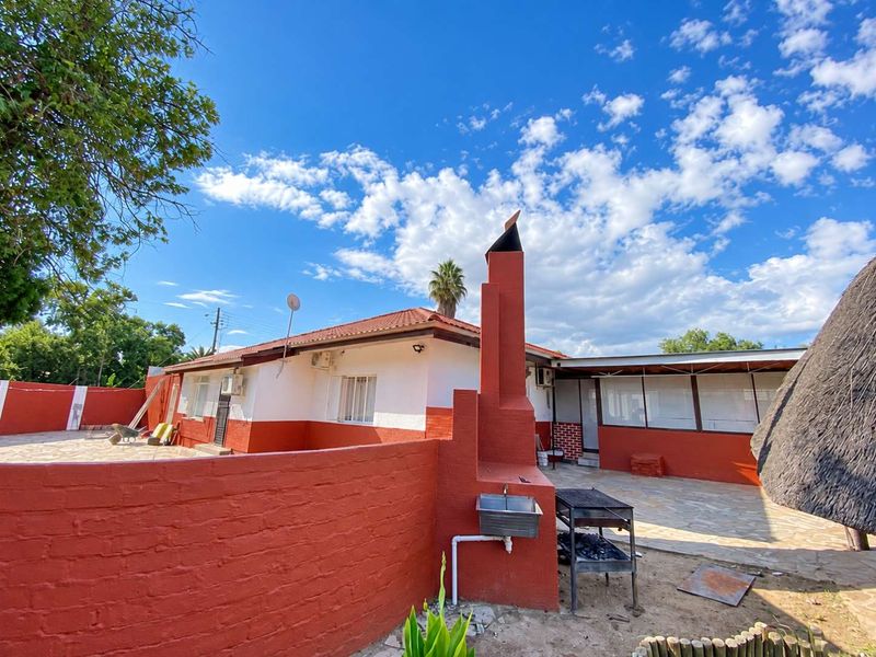 Rear exterior view of the guest house featuring a paved patio, built-in braai with chimney, outdoor sink, and a surrounding brick boundary wall.
