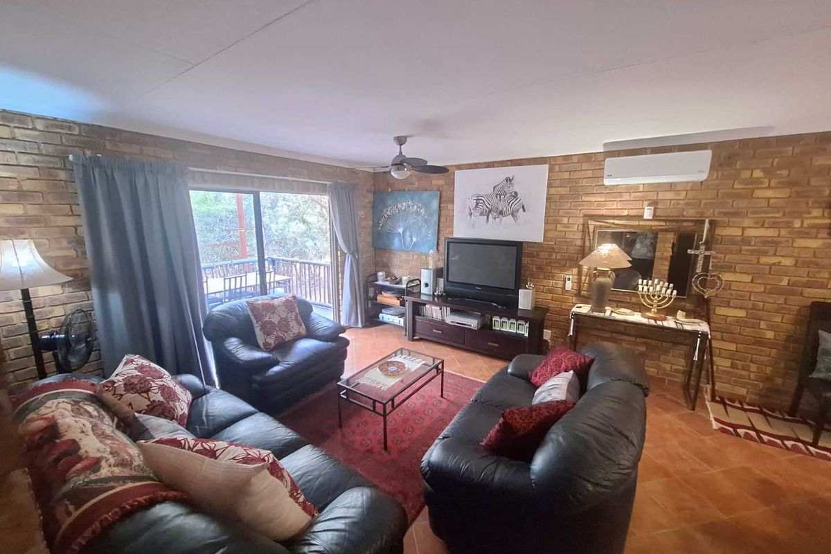 Spacious living room featuring exposed brick walls, terracotta floor tiles, a ceiling fan, and a wall-mounted air conditioning unit with sliding door access.