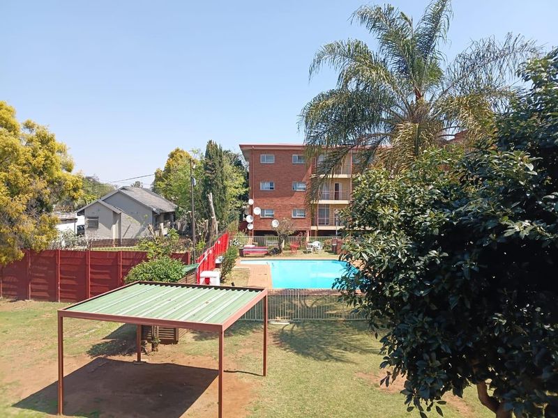 Communal outdoor area featuring a swimming pool, landscaped garden space, and a covered carport structure within the apartment complex grounds.