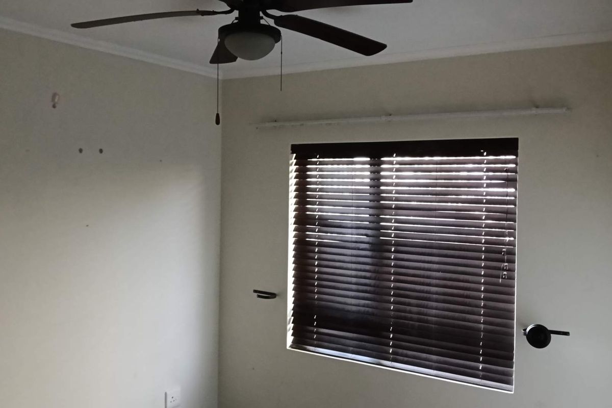 An empty bedroom featuring a ceiling fan, dark venetian blinds, and neutral wall finishes, ready for personalization.