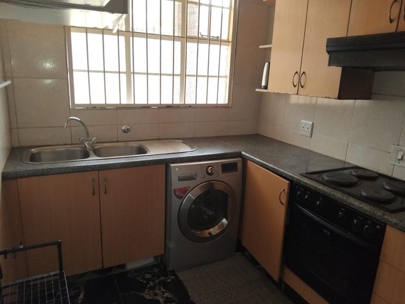 A functional kitchen featuring laminate cabinetry, a double bowl sink, built-in oven with electric hob, and a tiled backsplash with security bars on the window.