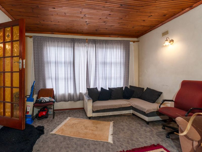 A living room featuring a timber tongue and groove ceiling, carpeted flooring, and a timber-framed glass entrance door.