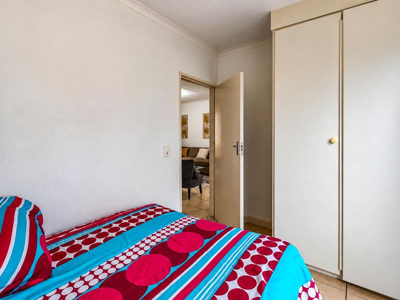 A bedroom featuring tiled flooring and a built-in wardrobe, with a doorway leading to an adjacent living area.