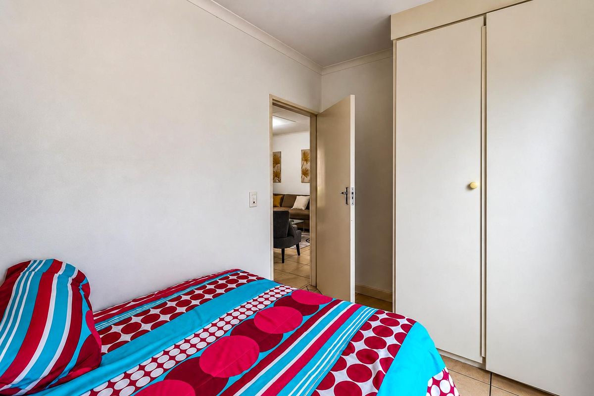 A bedroom featuring tiled flooring and a built-in wardrobe, with a doorway leading to an adjacent living area.
